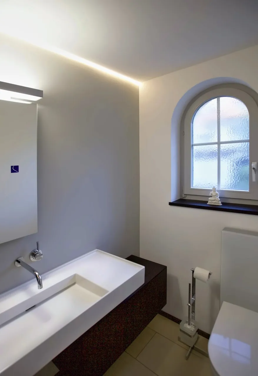 Rundbogenfenster, Lichtfuge und ein Waschtisch, der die Tiefe des Raums nutzt.