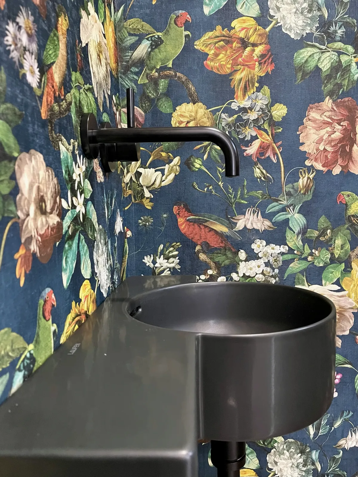 Schwarzes Waschbecken und Wandarmatur vor der Blumentapete